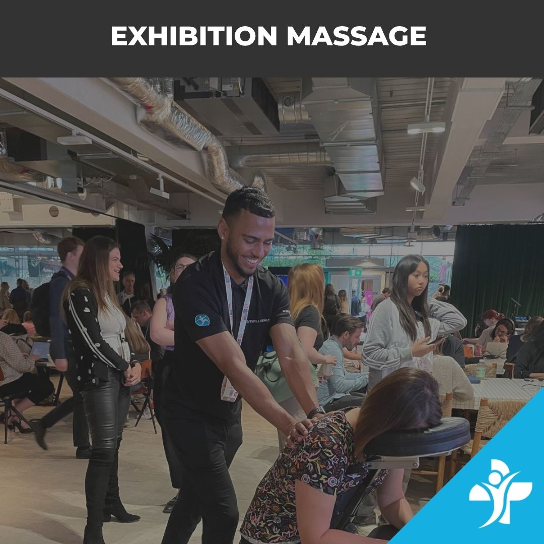 Man giving a back massage to a seated participant at an exhibition, with onlookers in a busy open venue.