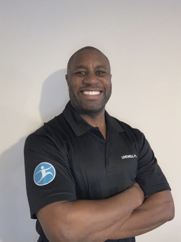 Smiling man with arms crossed, wearing a black polo with a blue emblem on the left sleeve, against a light background short portrait.