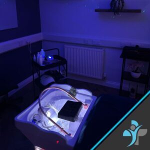 Blue-lit foot spa in a treatment room with hoses and a small cart holding bottles and supplies.